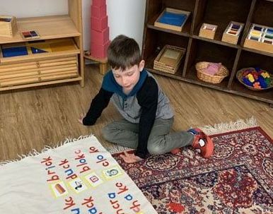 A young boy is sitting on the floor playing with a rug.