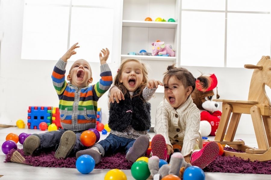 Three children are sitting on the floor playing with toys.