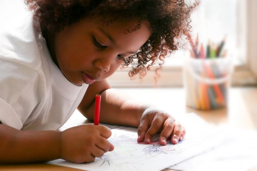 A young boy is sitting at a table drawing with a red marker.