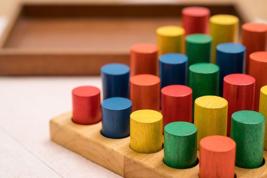 A wooden tray filled with colorful wooden cylinders on a table.