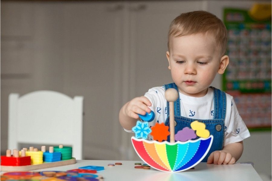 A little boy is playing with a rainbow umbrella toy on a table.