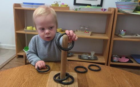 A young boy is playing with rings on a wooden table.