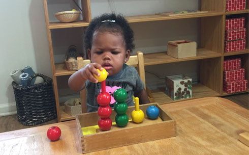 A little girl is sitting at a table playing with a wooden toy.