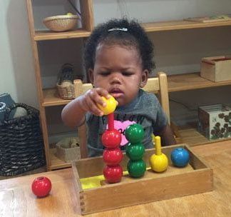 A little girl is sitting at a table playing with a wooden toy.