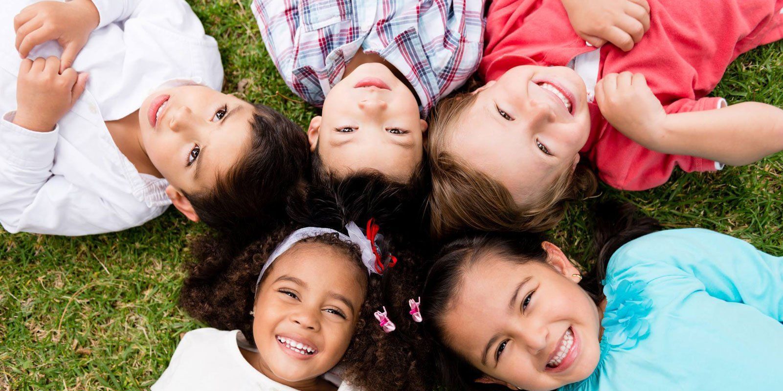 A group of children are laying in a circle on the grass and smiling.