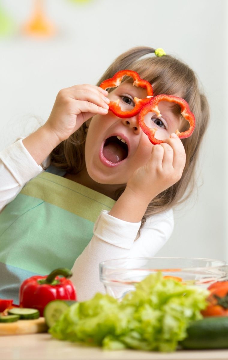 A little girl is wearing glasses made of peppers on her face.