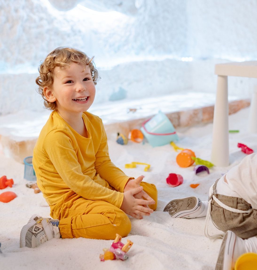 A little boy in a yellow shirt is sitting on the floor playing with toys.