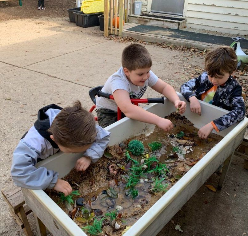 Three young boys are playing with toys in a sandbox