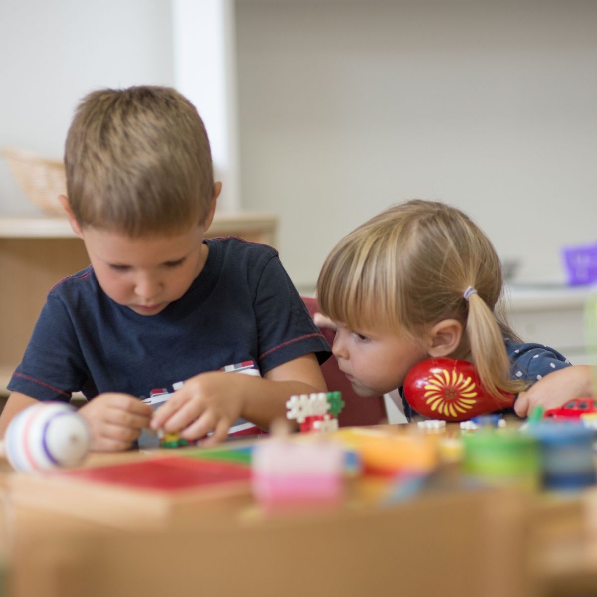 A boy and a girl are playing with toys at a table