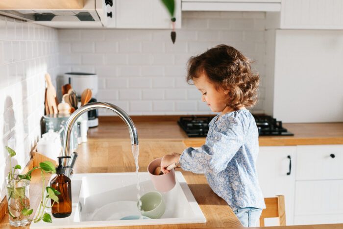 A little girl is washing dishes in a kitchen sink.