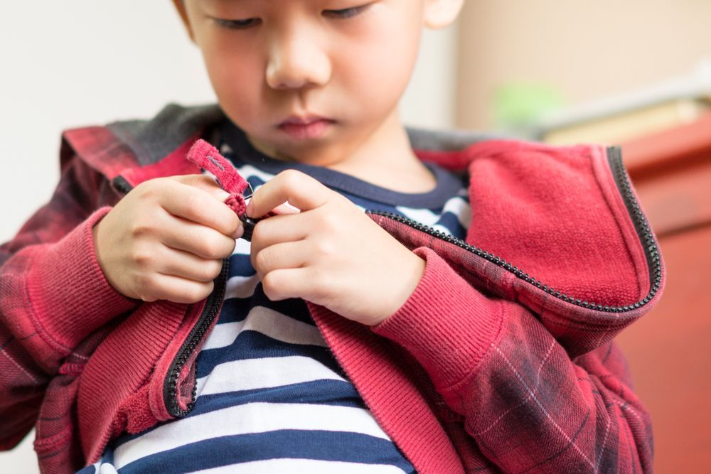 Preschooler zipping up his sweatshirt as part of learning practical life skills at a Montessori