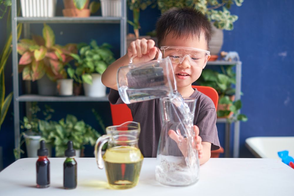 A young boy is pouring water into a glass jar.