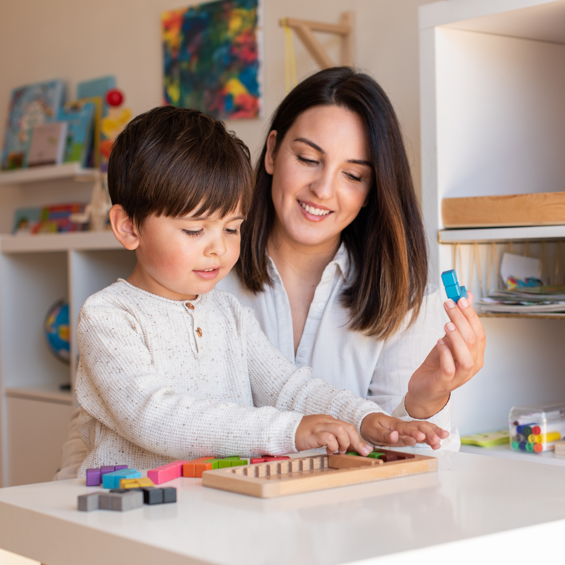 A woman and a child are playing with blocks at a table.