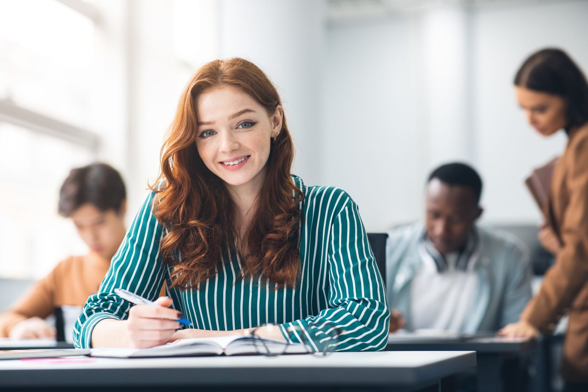 A woman is sitting at a desk in a classroom with other students.