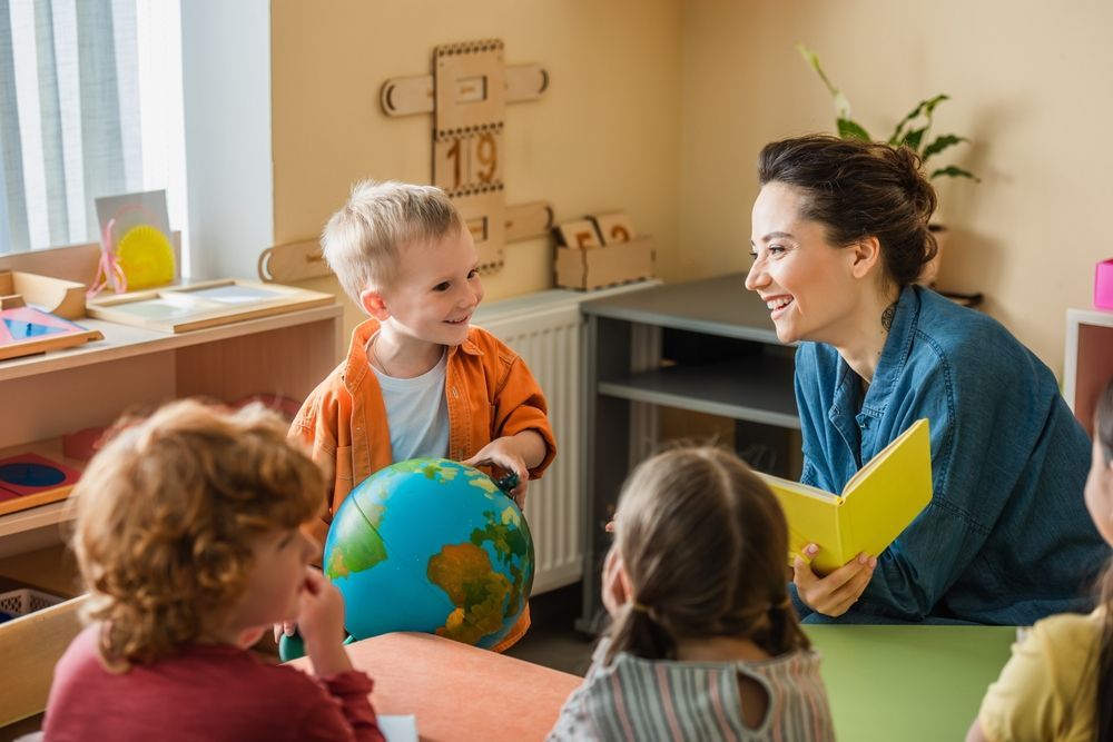 A teacher is reading a book to a group of children while holding a globe.