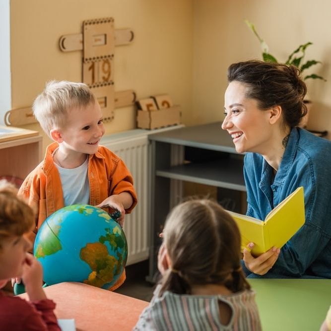 A woman is holding a book and a child is holding a globe.