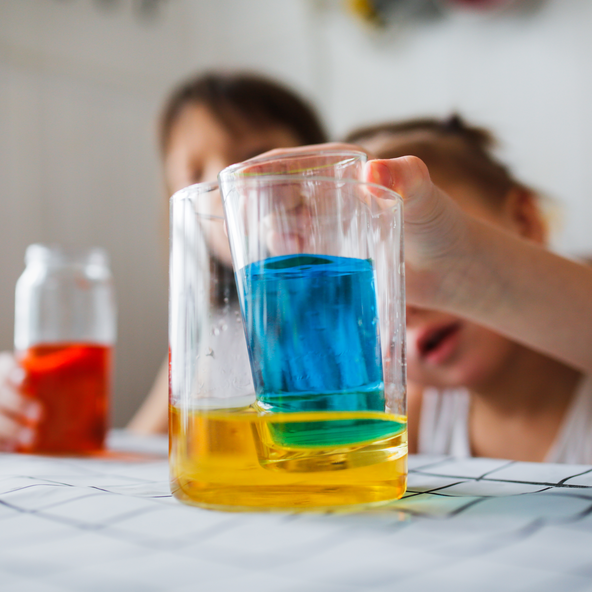 A person is holding a glass with blue and yellow liquid in it.