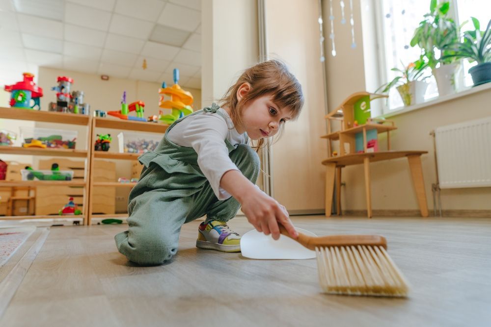 preschooler sweeping up crumbs into a dustpan to help build practical life skills