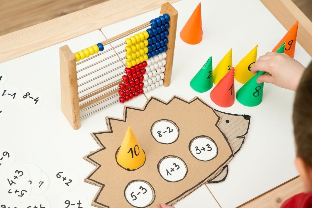 A child is playing with a cardboard hedgehog and a wooden abacus