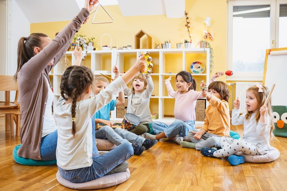 A group of children are sitting on the floor in a circle with their hands in the air.