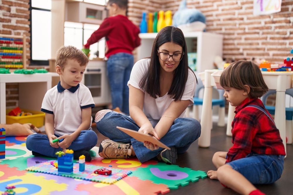 A preschool teacher is sitting on the floor with two young boys learning and playing