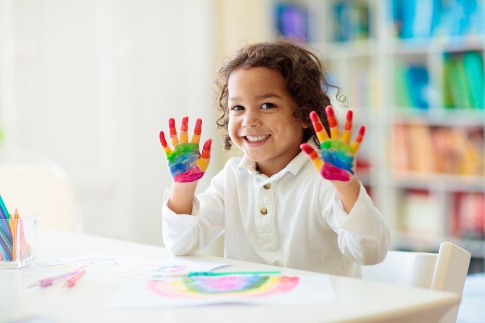 A little girl is sitting at a table with her hands painted in different colors.