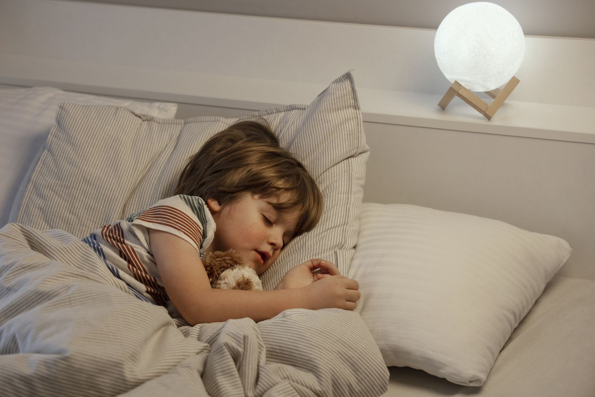 A little boy is sleeping in a bed with a night light to help the toddler stay in bed