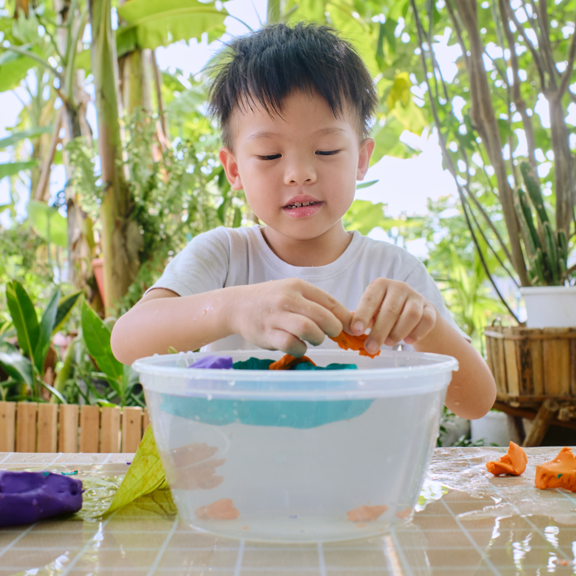 A young boy is playing with a plastic bowl of water.