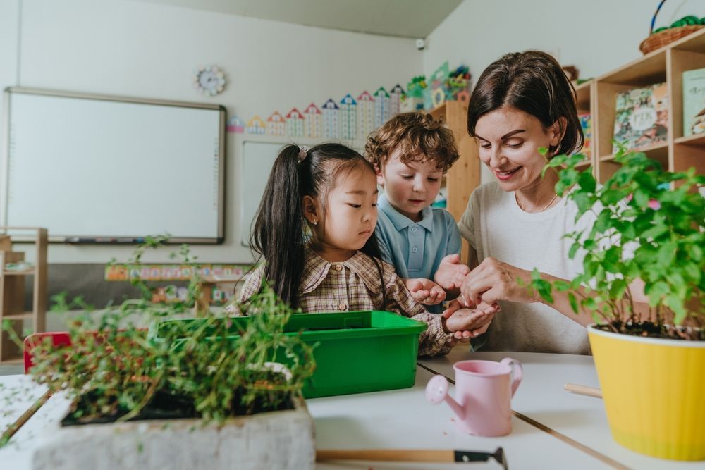 A teacher is teaching two children how to plant plants in a classroom.