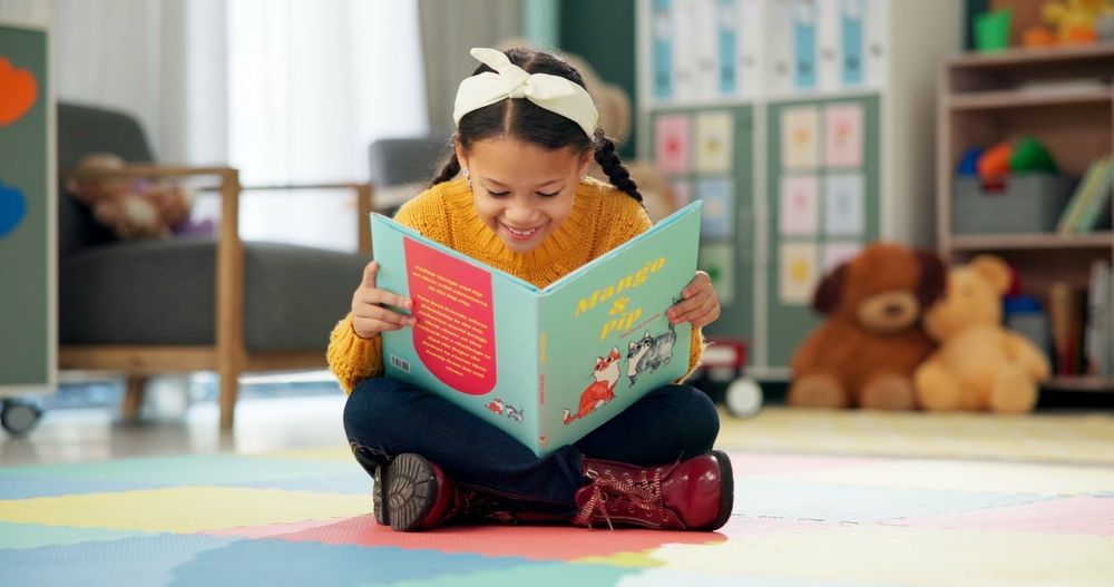 A little girl is sitting on the floor reading a book.