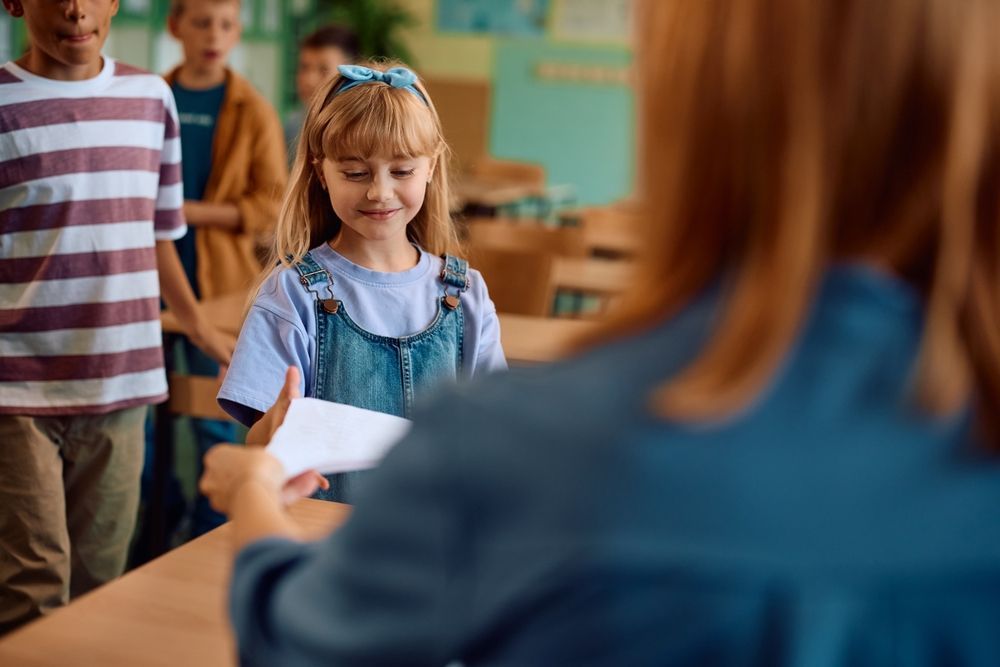 A teacher is giving a piece of paper to a young girl in a classroom.