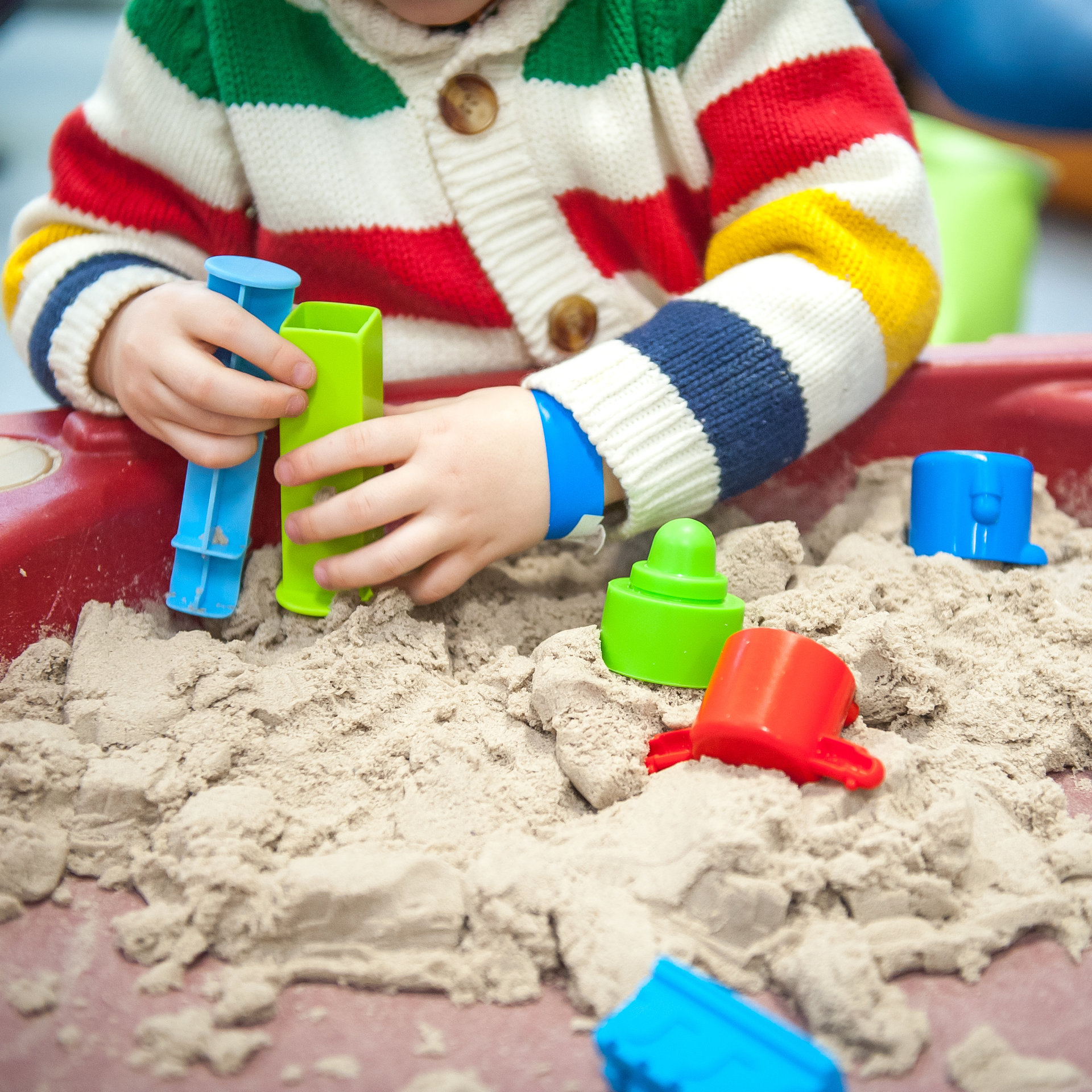 A child in a striped sweater is playing in a sandbox