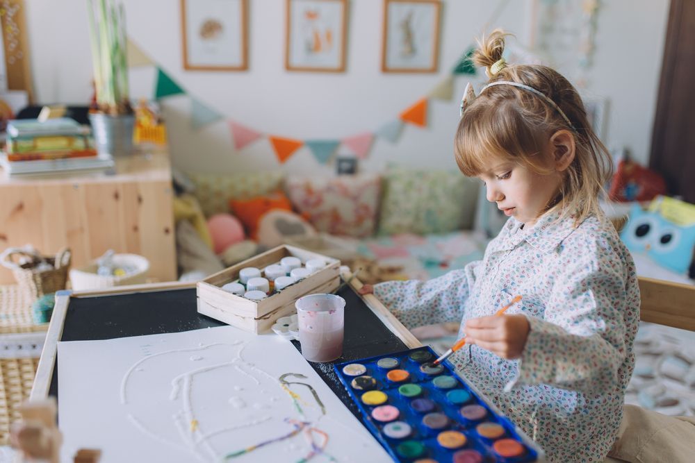 A little girl is sitting at a table painting with watercolors.