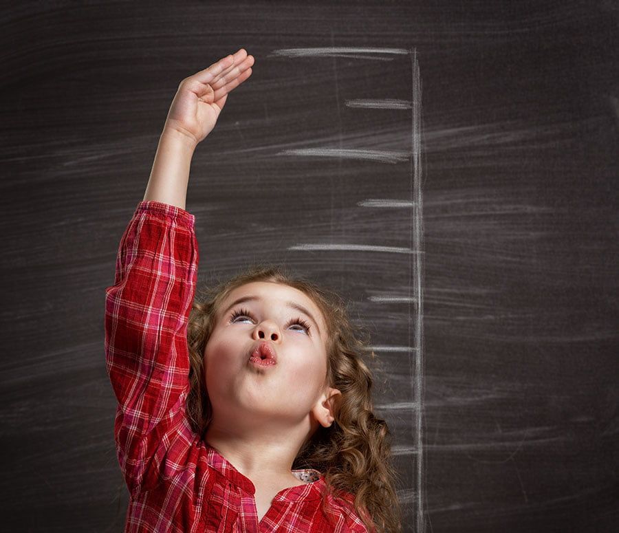 A little girl is measuring her height on a blackboard.