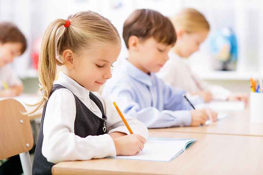 A group of children are sitting at desks in a classroom writing on papers.