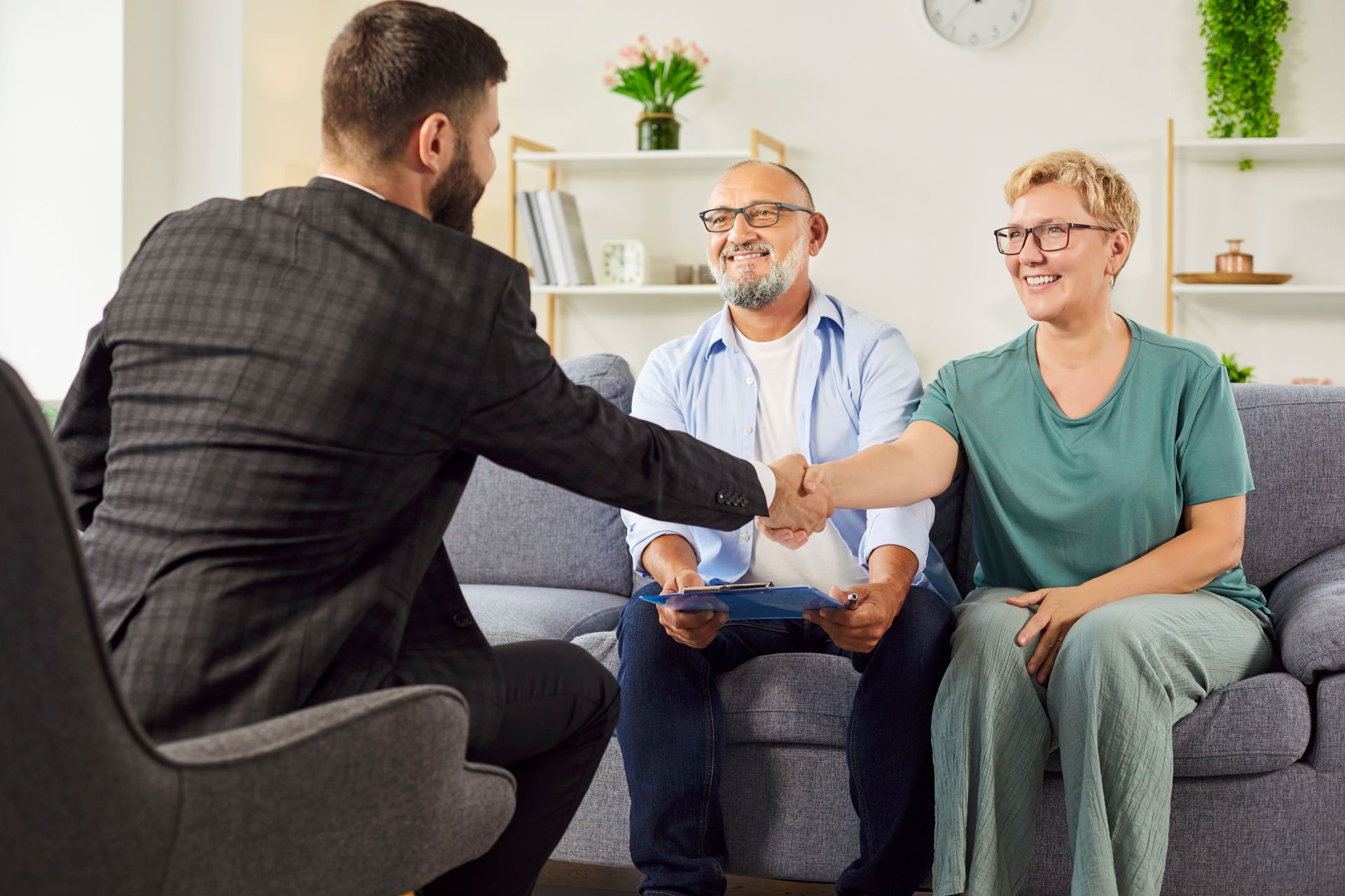 Man in suit shakes hands with a couple on a sofa. They are smiling in a home setting. Man in suit shakes hands with a couple on a sofa. They are smiling in a home setting.