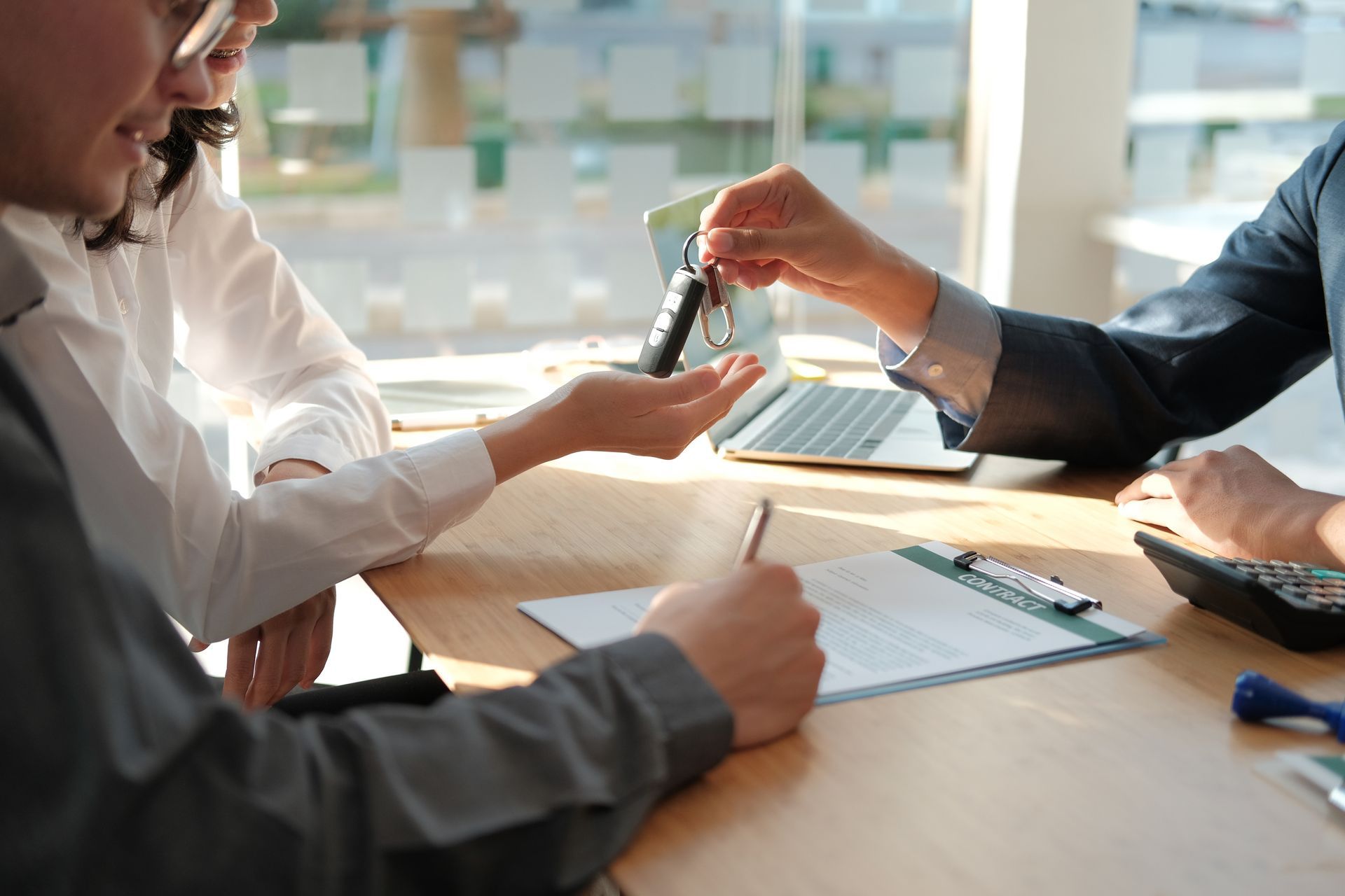 Person handing car keys to couple at a desk with a signed document and calculator.