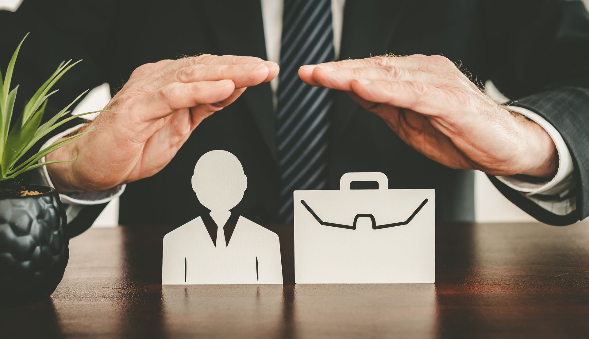 Businessperson's hands protect a cutout person and briefcase. Businessperson's hands protect a cutout person and briefcase.