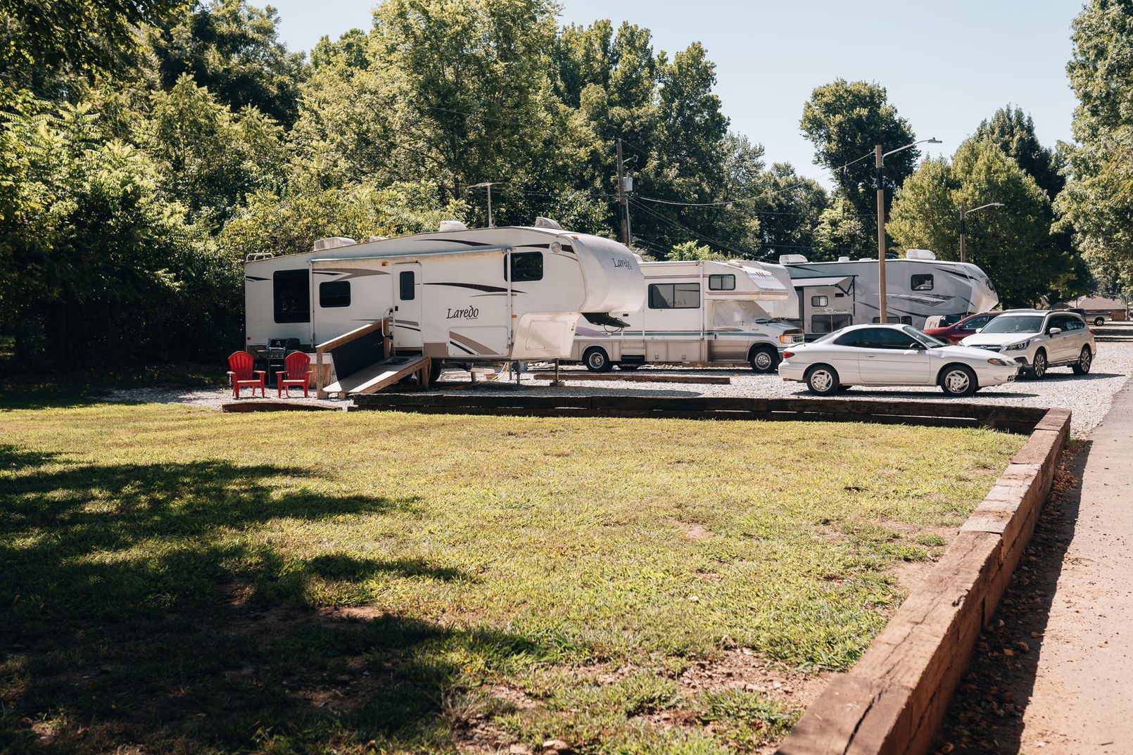 Aerial view of a wooded campground featuring several parked recreational vehicles and cars on a gravel lot.