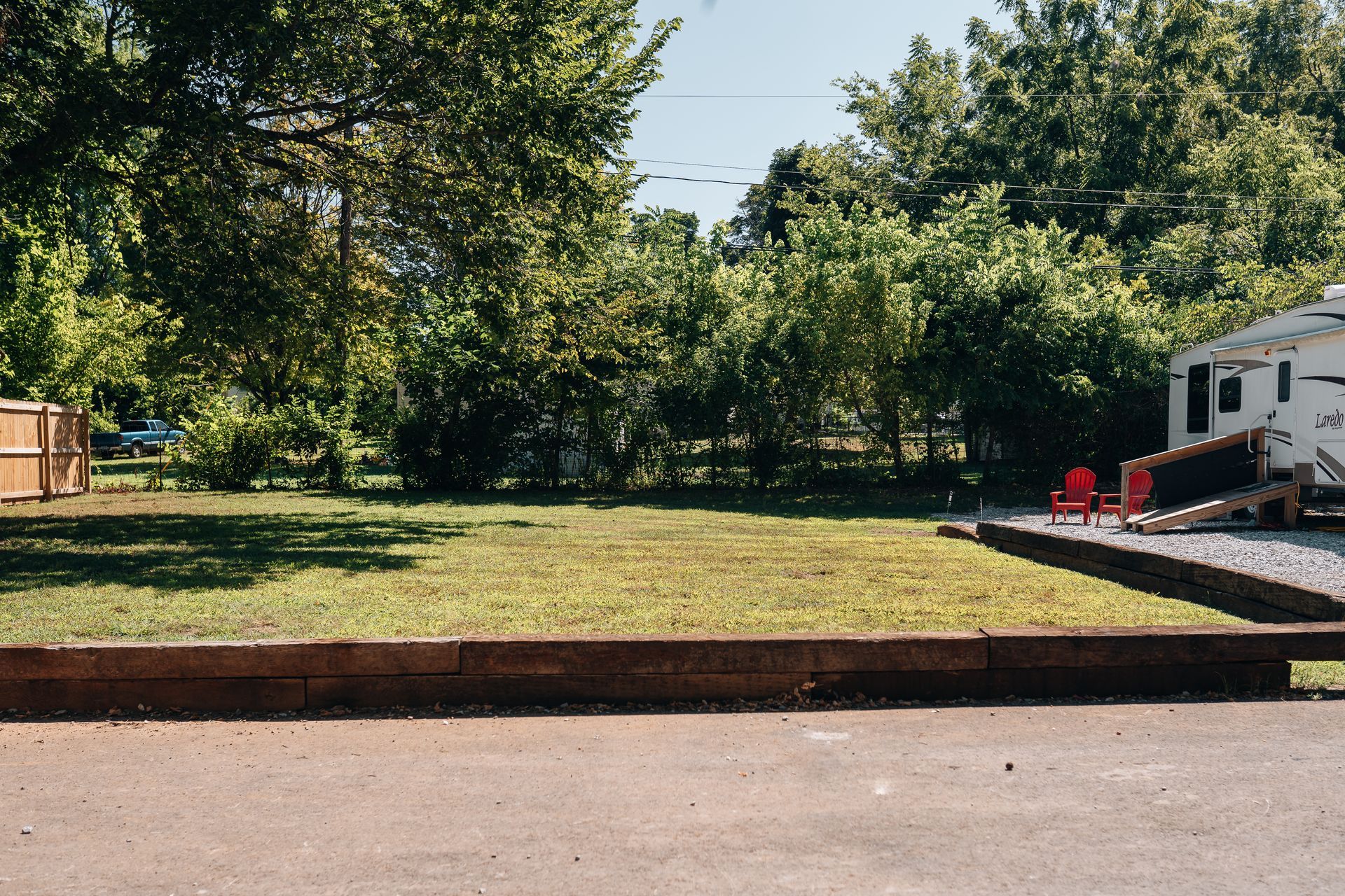 A grassy lot with a low retaining wall in the foreground and a parked camper trailer to the right.