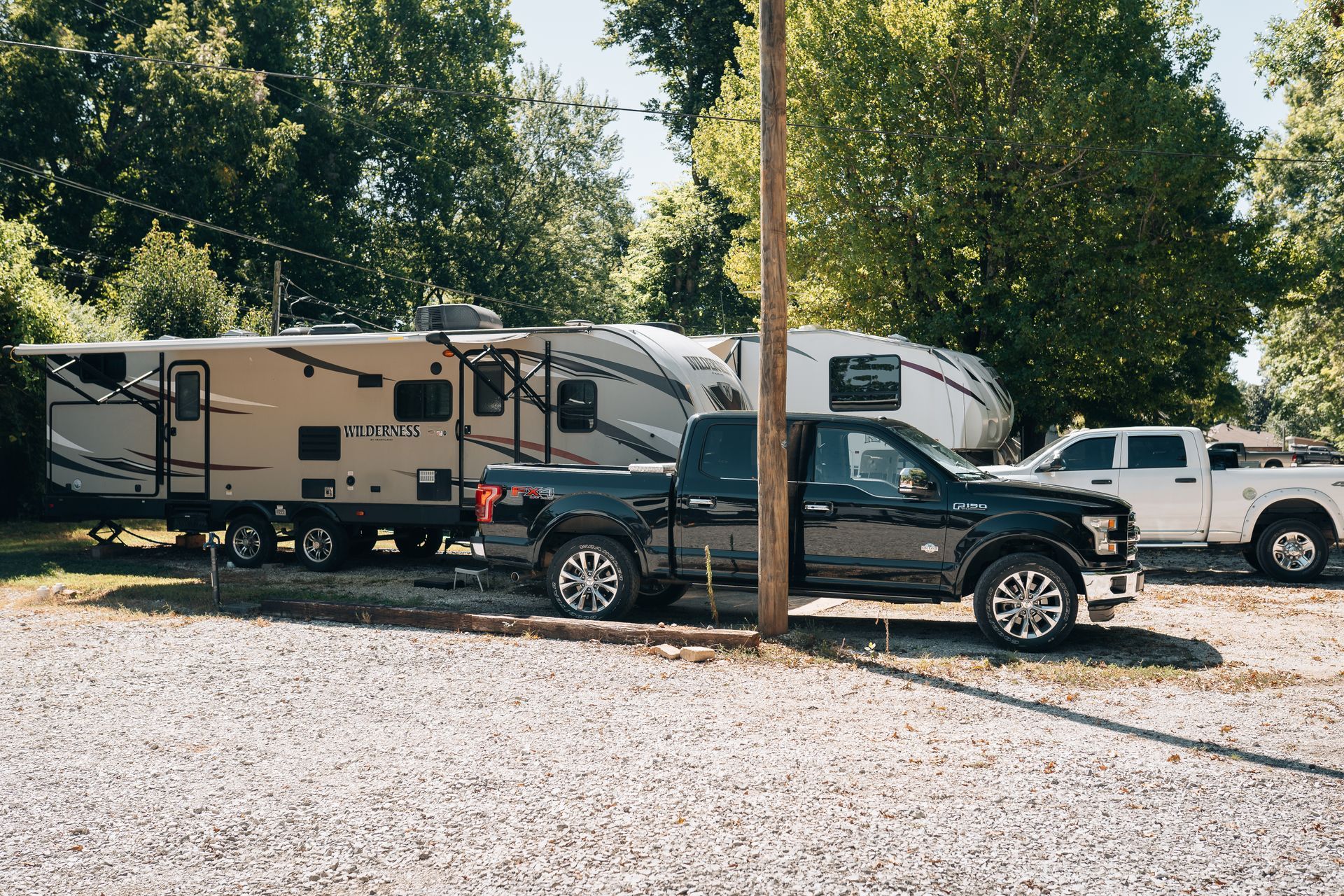 A black pickup truck parked in a gravel lot next to two recreational vehicles, with trees in the background.