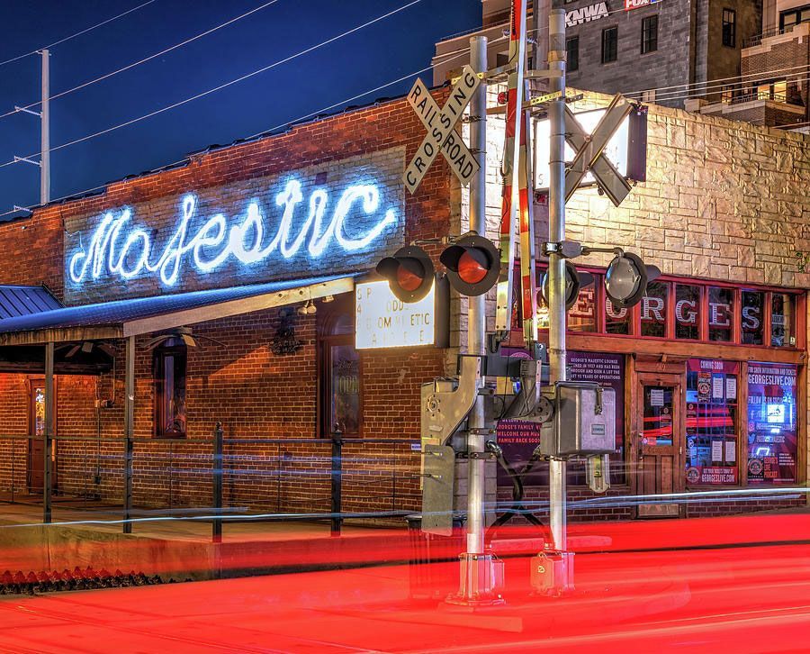 A night scene of the Majestic building with neon signage, a railroad crossing signal, and red light trails in the street.