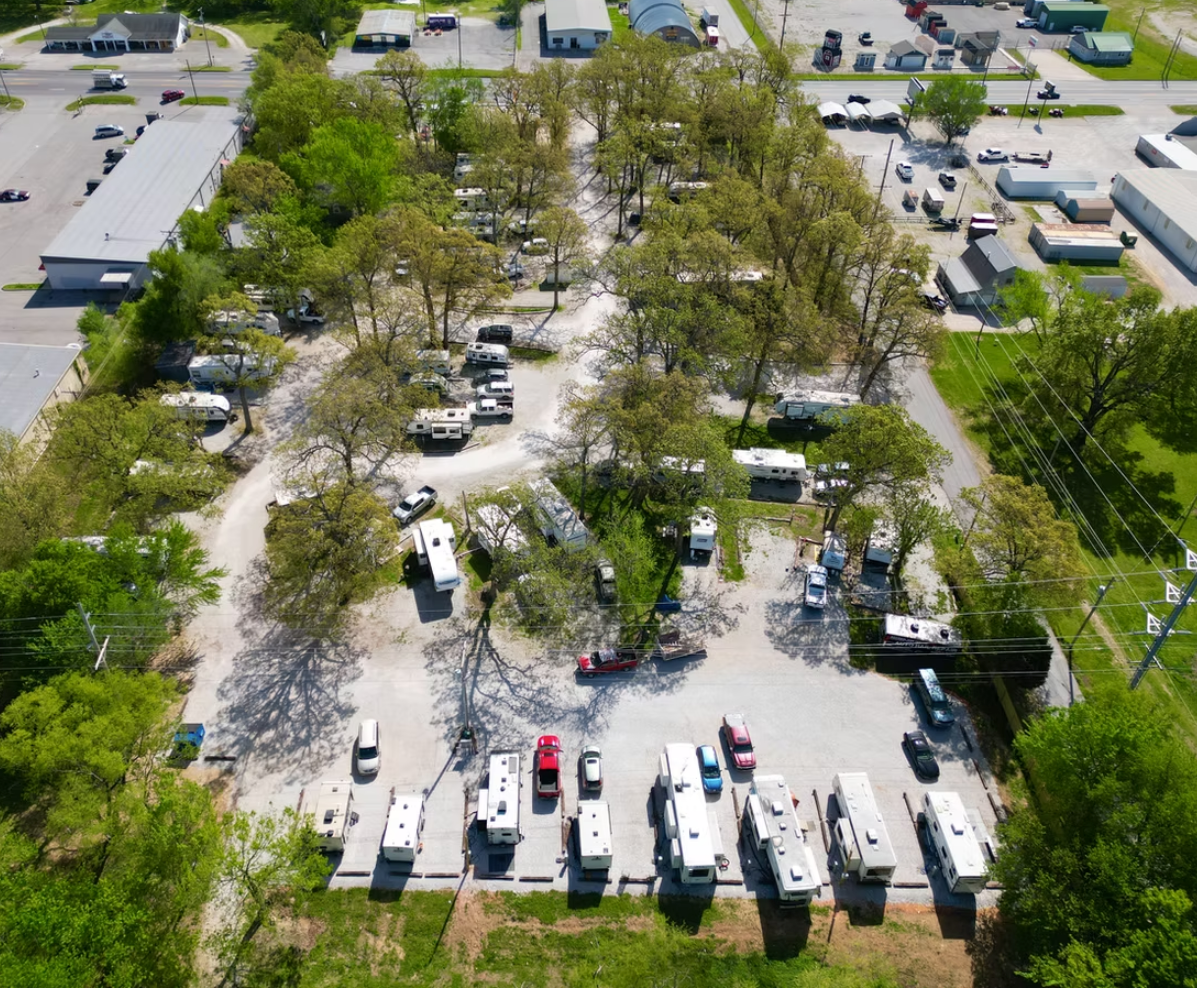 Aerial view of an RV park with multiple parked campers and vehicles on gravel lots among trees.