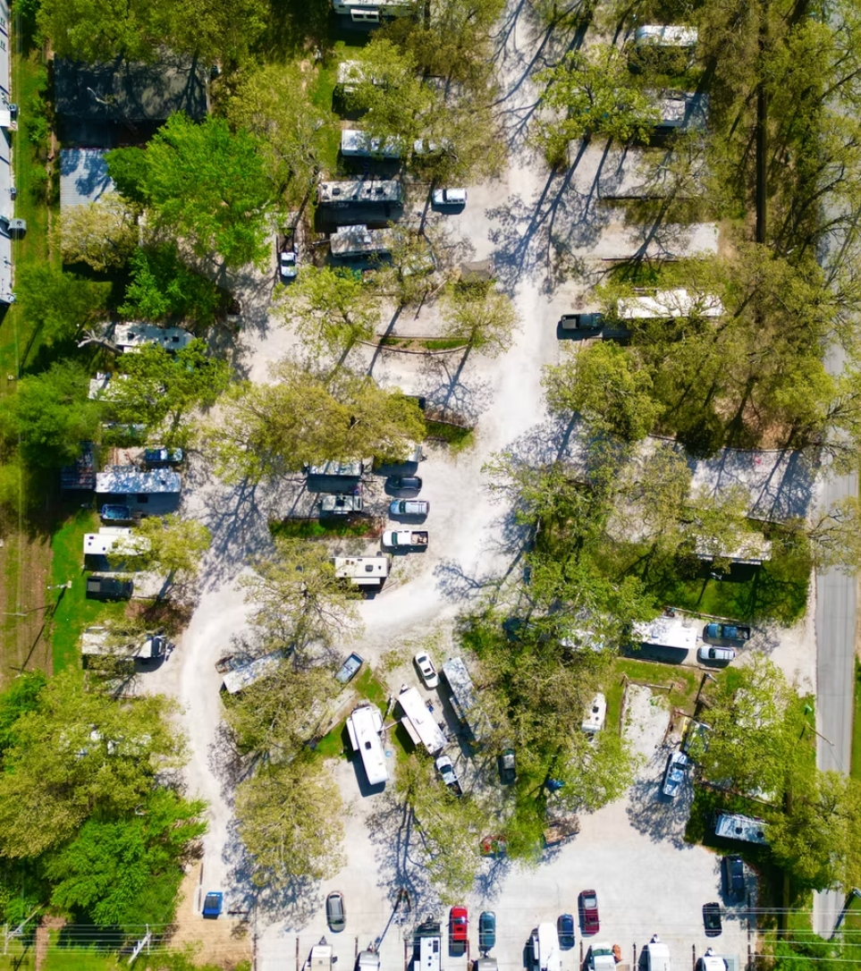 Aerial view of an RV park with several campers parked among trees and a gravel road winding through the campground.
