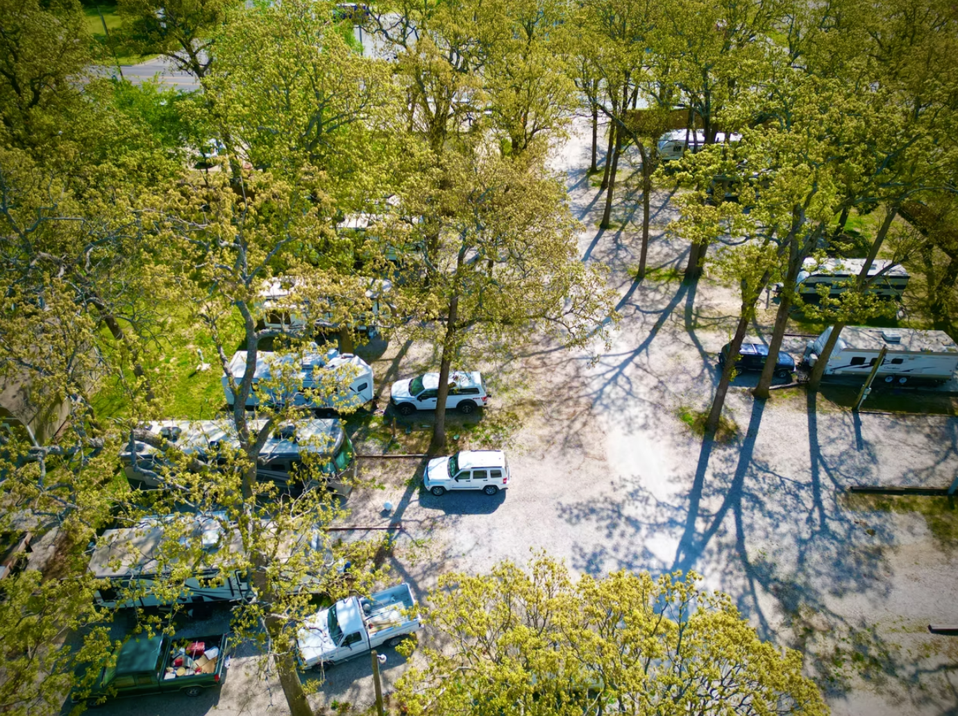 An aerial view of a wooded campsite with several parked RVs, campers, and vehicles scattered among the trees.
