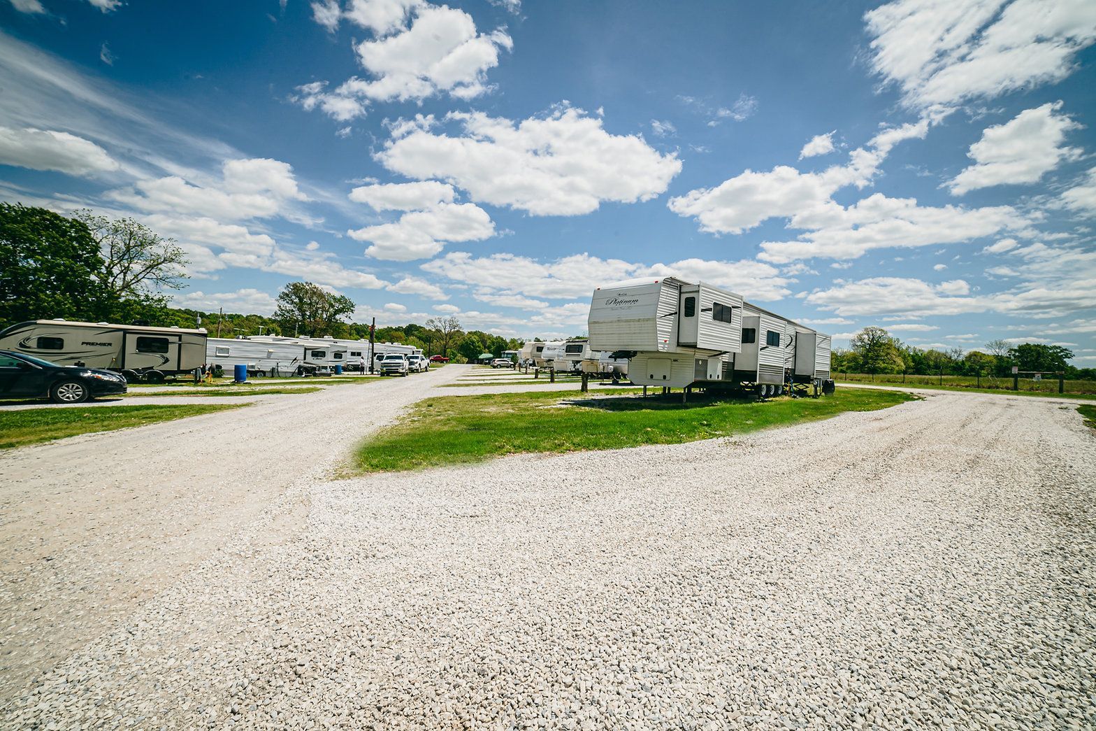 Several RVs parked on a gravel lot under a bright blue, cloudy sky.