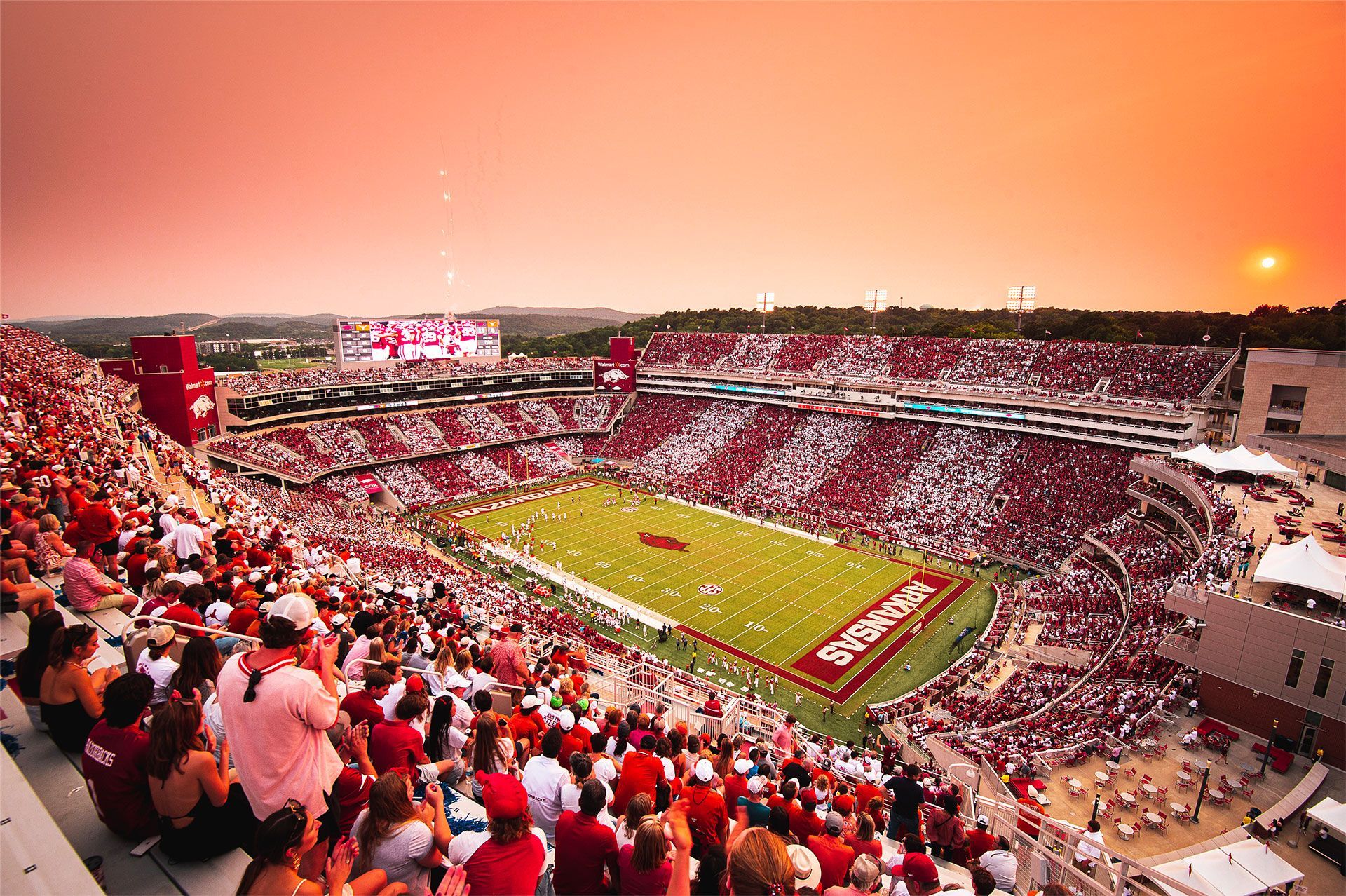 A high-angle view of a crowded football stadium at sunset with spectators wearing red and white in a vibrant arena.