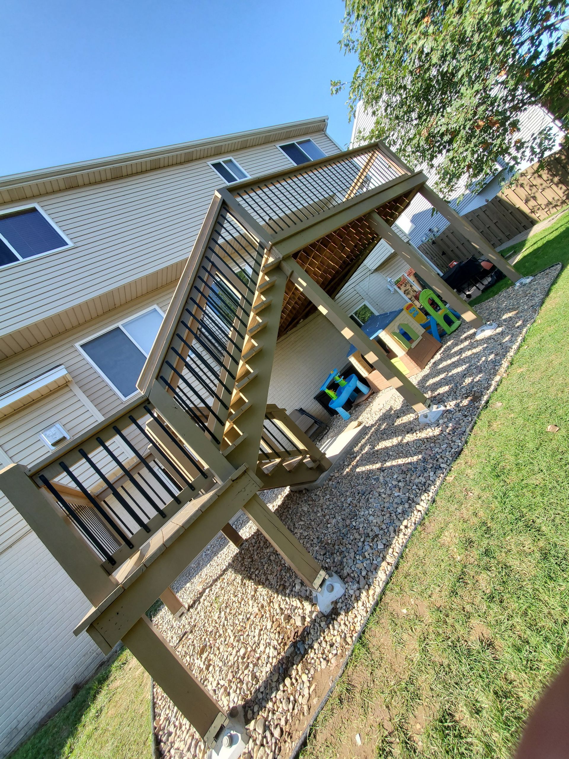 A wooden deck with stairs leading up to it is in the backyard of a house.