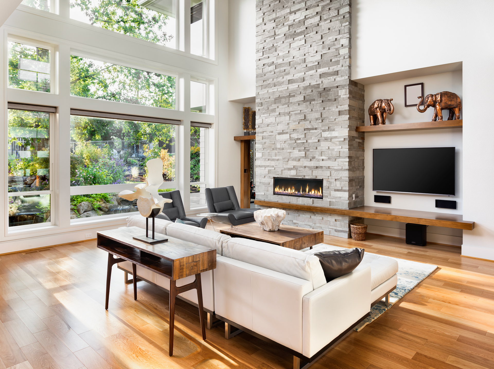 A living room with a couch , fireplace , television and lots of windows.