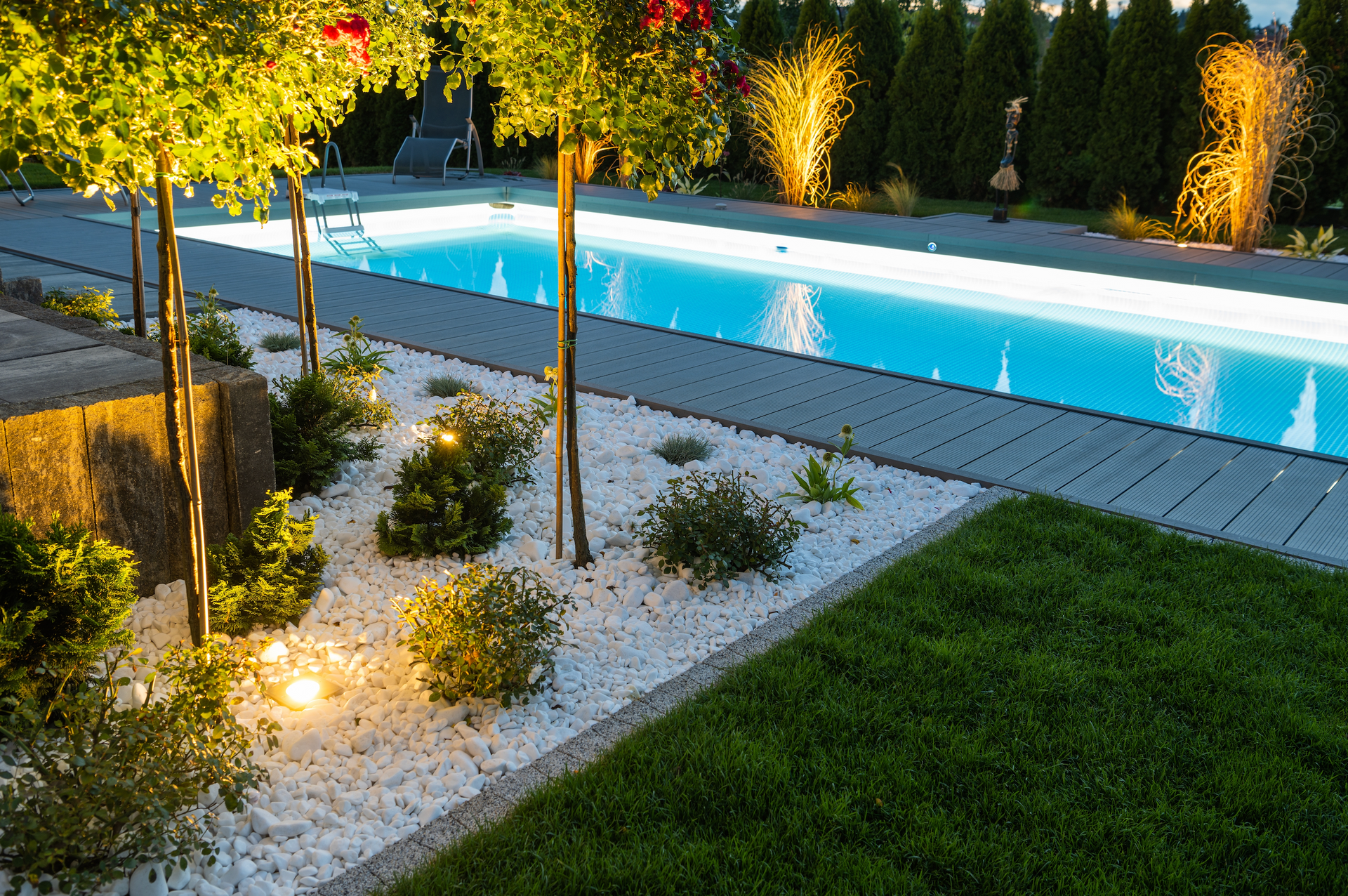A large swimming pool is surrounded by trees and gravel in a backyard.